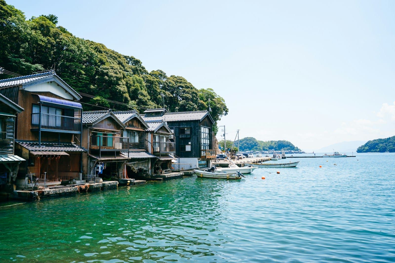 Funaya boathouses lining the shore of calm, clear Ine Bay under a summer sky