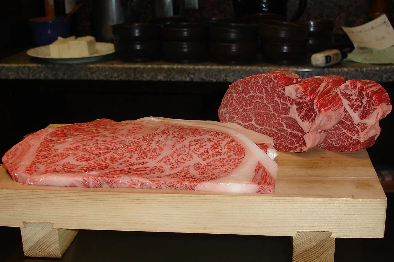 Two heavily marbled raw Kobe beef cuts on a wooden serving board
