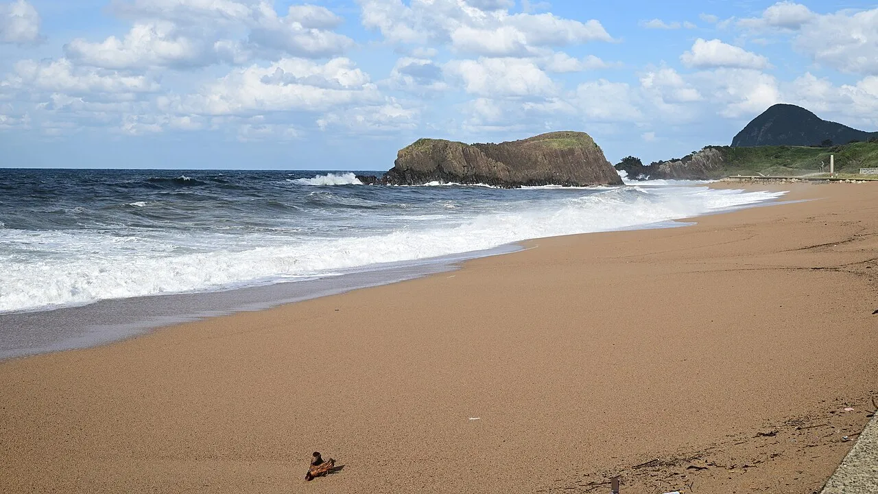 A wide sandy beach on the Sea of Japan coast at Taiza in Kyotango, with rolling surf and the Tateiwa rock under a blue sky